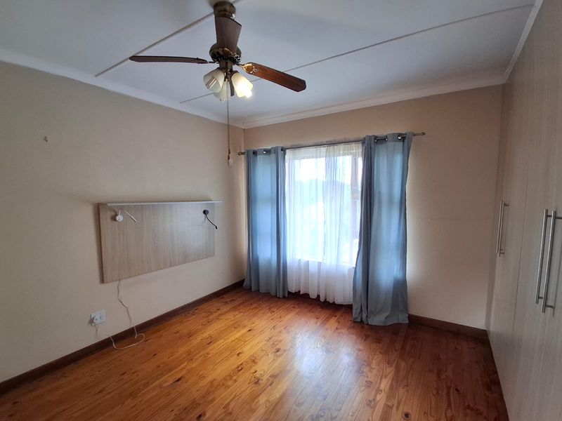 A spacious bedroom featuring polished timber flooring, built-in cupboards, a ceiling fan, and a wall-mounted headboard panel, offering a clean and neutral canvas.