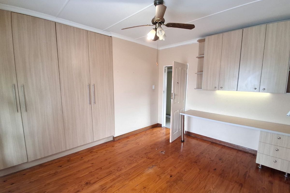 Spacious bedroom featuring polished timber flooring, extensive built-in cupboards, and a dedicated built-in desk area with overhead storage.
