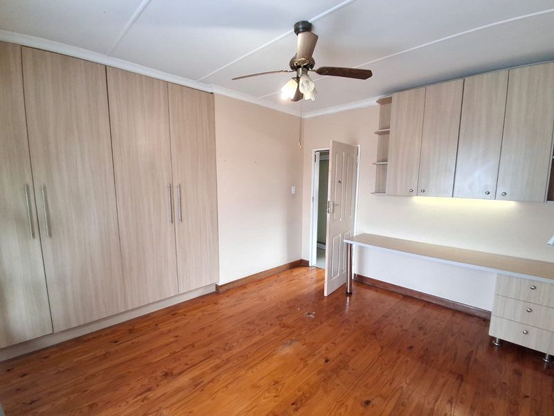 Spacious bedroom featuring polished timber flooring, extensive built-in cupboards, and a dedicated built-in desk area with overhead storage.