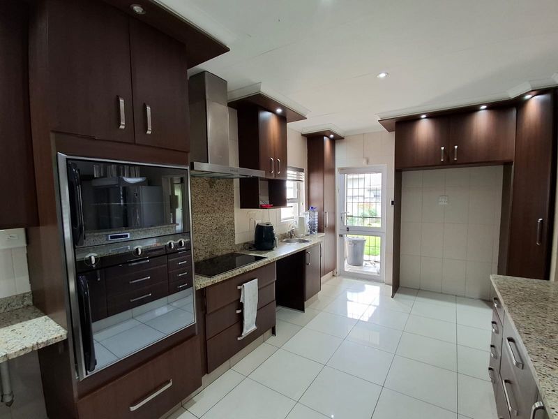 Modern kitchen featuring dark wood cabinetry, granite countertops, built-in oven, extractor fan, and tiled flooring with direct access to the rear exterior.