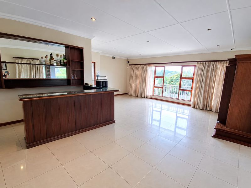 Spacious living area featuring a built-in wooden bar, polished tile flooring, and large windows providing natural light and scenic views.