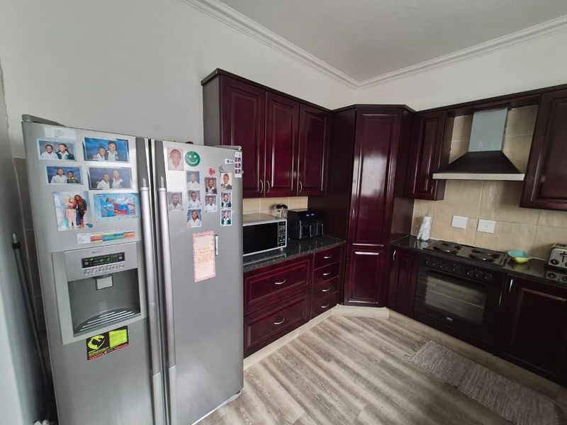 A functional kitchen featuring dark wood cabinetry, granite countertops, built-in oven, hob, and extractor fan with a tiled backsplash and laminate flooring.