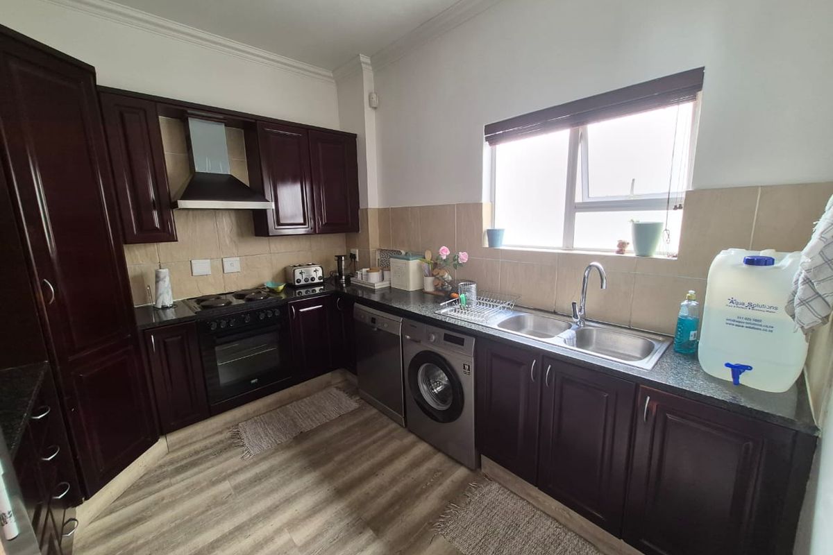 A functional kitchen featuring dark wood cabinetry, granite countertops, a built-in oven, hob, extractor fan, and a stainless steel sink with tiled backsplash.