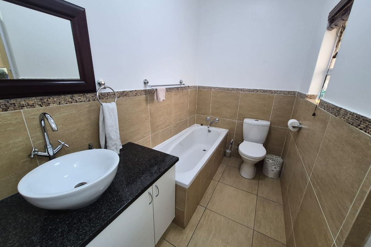 A well-maintained bathroom featuring a vessel sink on a granite vanity, a bathtub, and neutral-toned wall and floor tiling with a decorative mosaic border.