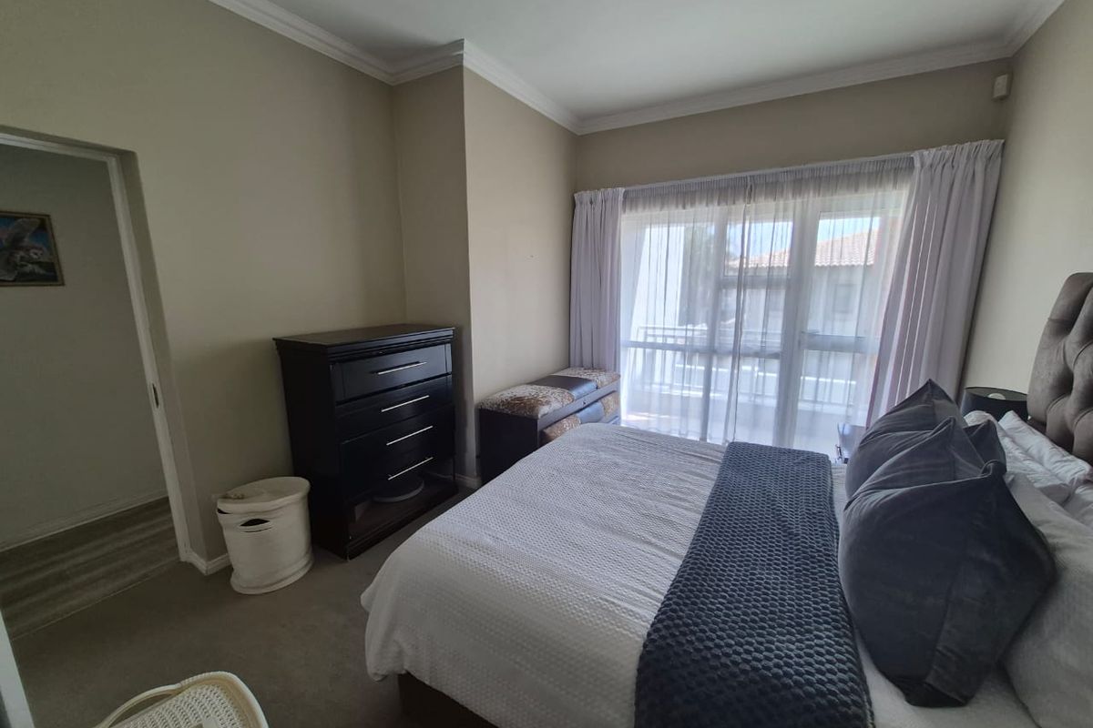 A well-maintained bedroom featuring neutral wall tones, crown molding, carpet flooring, and a large sliding glass door providing access to a balcony.