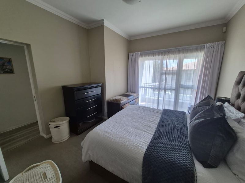 A well-maintained bedroom featuring neutral wall tones, crown molding, carpet flooring, and a large sliding glass door providing access to a balcony.