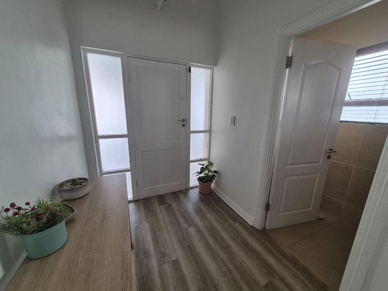 A bright entrance foyer featuring modern laminate flooring, a panelled front door with frosted glass sidelights, and neutral wall finishes.