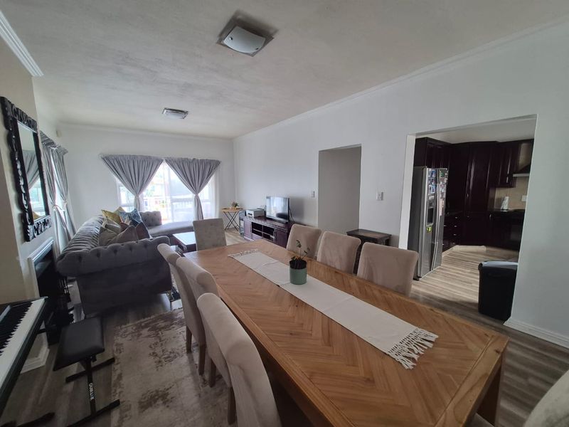 Spacious open-plan living and dining area featuring laminate flooring, coved ceilings, and a seamless transition into the adjacent dark-toned kitchen.