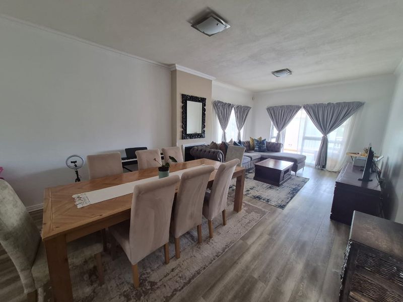 Spacious open-plan living and dining area featuring laminate flooring, neutral walls, and sliding glass doors leading to an outdoor space.