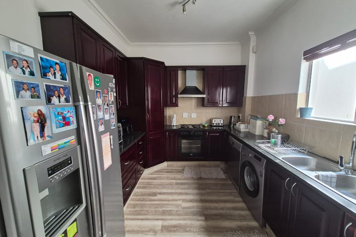 A functional kitchen featuring dark wood cabinetry, granite countertops, built-in oven with extractor fan, and a stainless steel sink with tiled backsplash.