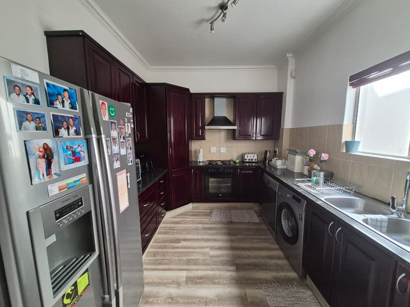 A functional kitchen featuring dark wood cabinetry, granite countertops, built-in oven with extractor fan, and a stainless steel sink with tiled backsplash.