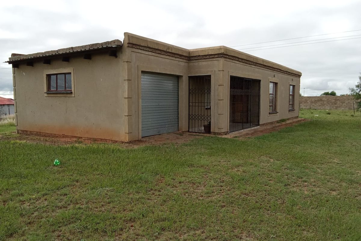 Single-story residential house featuring a roller garage door, security gates, and plastered exterior walls, situated on a large open plot.