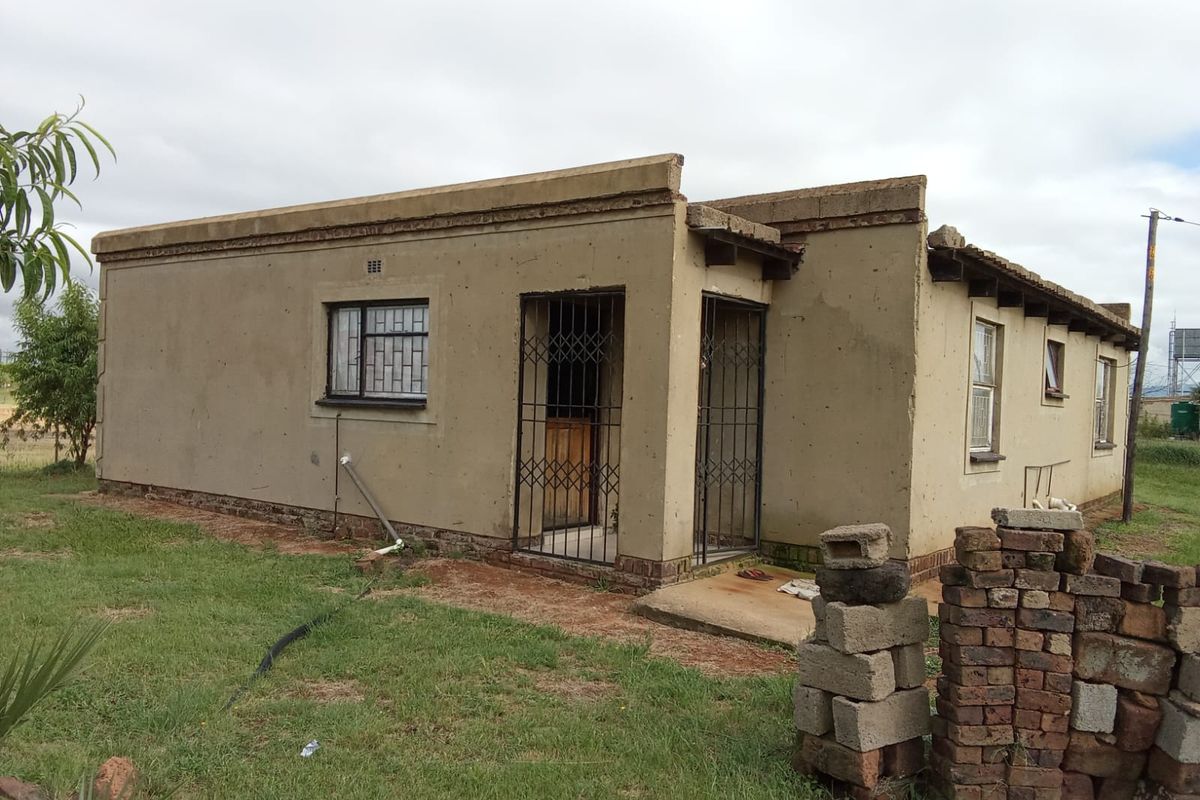 A single-story residential property featuring plastered exterior walls, security gates, and metal window frames, currently requiring significant maintenance and exterior finishing.