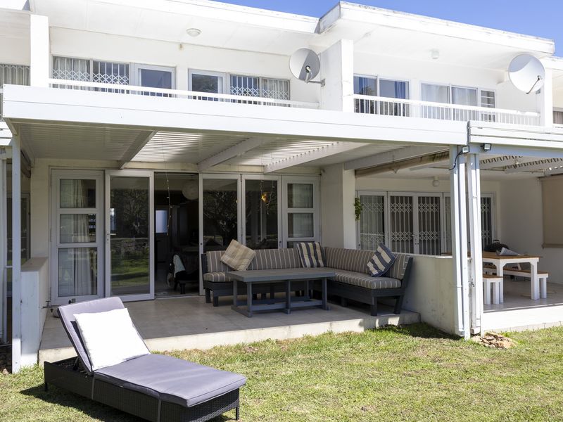 Rear view of the townhouse featuring a covered patio area with tiled flooring, sliding glass doors, and security gates leading to a private garden.