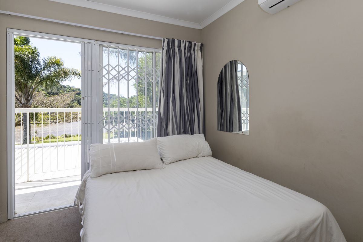 A well-maintained bedroom featuring carpeted flooring, an air conditioning unit, and a sliding glass door providing access to a private balcony.