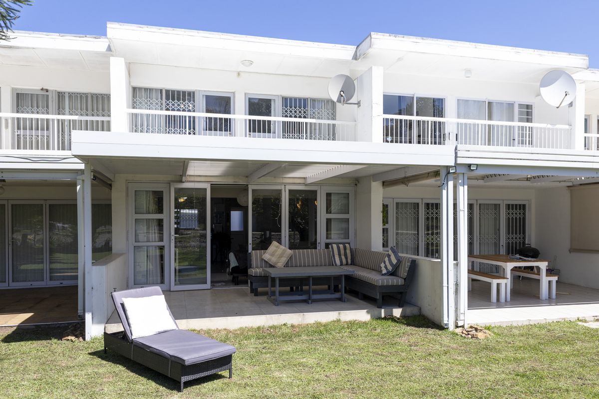 Rear view of a townhouse featuring a covered patio area, upper-level balconies, and sliding glass doors with security gates.