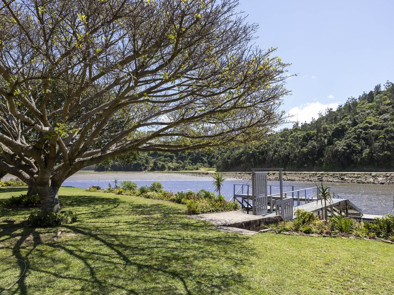 Scenic waterfront view featuring a private jetty, well-maintained lawn, and mature trees overlooking the river and natural landscape.