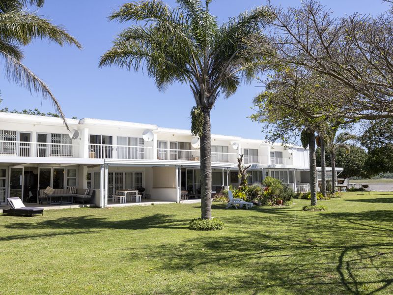 Rear view of a townhouse complex featuring ground floor covered patios, upper level balconies, and a well-maintained communal garden area.
