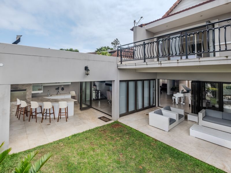 Spacious covered patio area featuring a built-in braai, stone breakfast bar, and seamless access to the garden through folding glass doors.