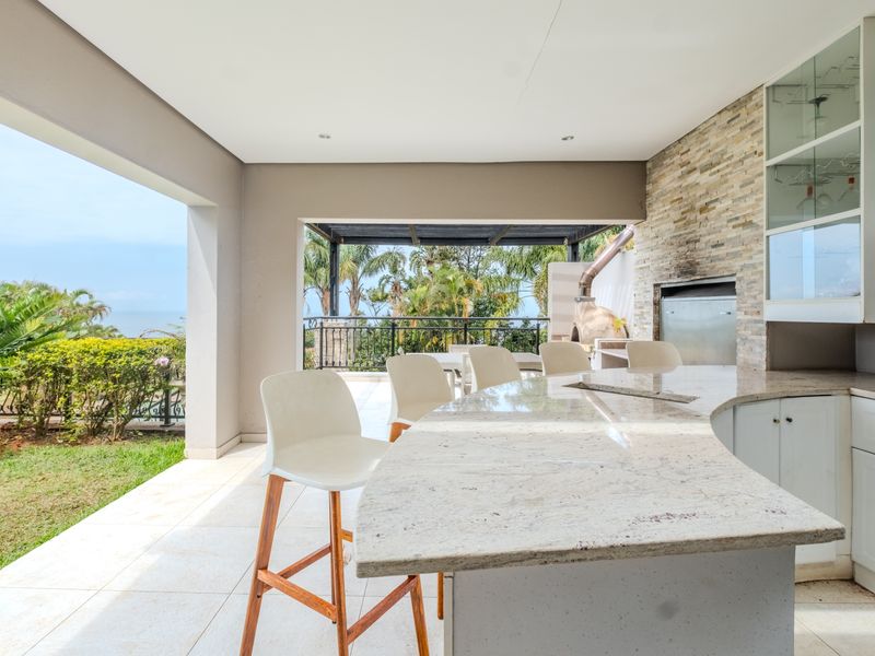 Covered outdoor patio featuring a built-in braai, stone-clad feature wall, granite breakfast bar, and direct access to the garden and scenic views.