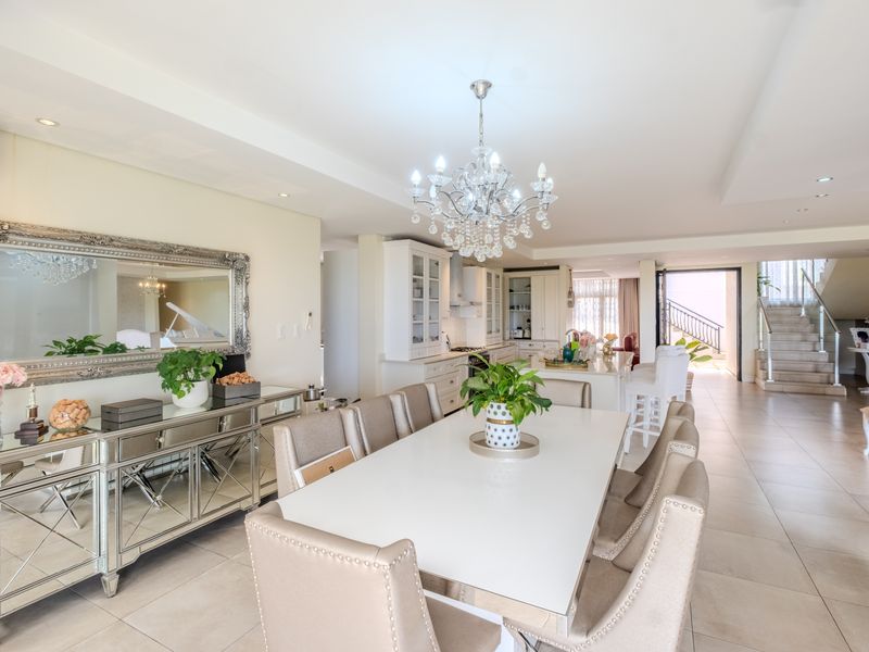 Spacious open-plan living and dining area featuring a modern kitchen with island, elegant chandelier lighting, and a staircase with glass balustrade.