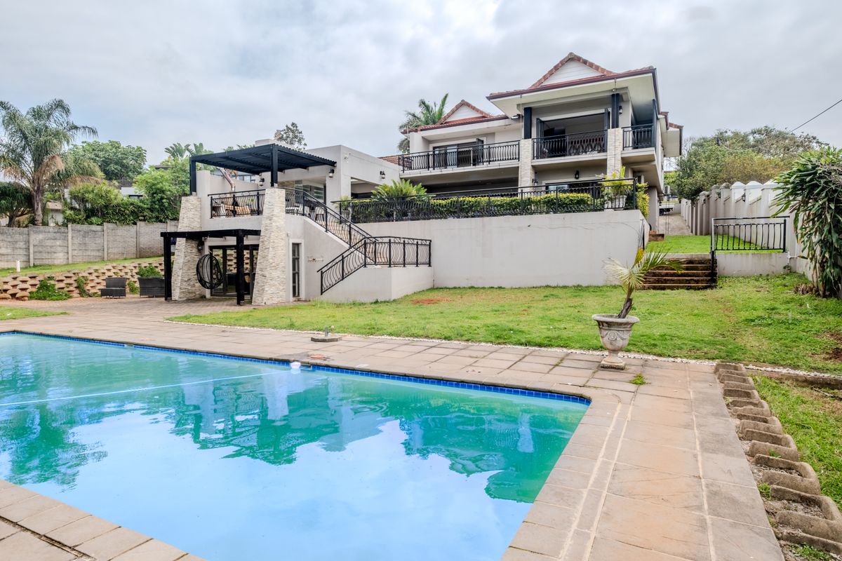 Rear view of a multi-story residence featuring a swimming pool, raised patio with pergola, and balcony access, set within a landscaped garden.
