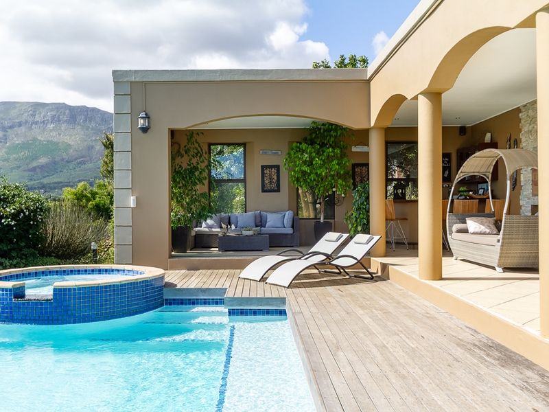 Spacious outdoor entertainment area featuring a swimming pool with tiled surround, wooden decking, and a covered patio with stone columns and mountain views.