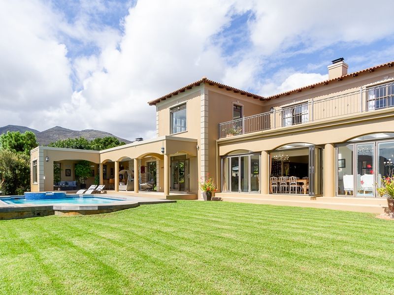 Spacious rear exterior featuring a well-maintained lawn, swimming pool, covered patio area, and a large balcony overlooking the garden and mountain views.