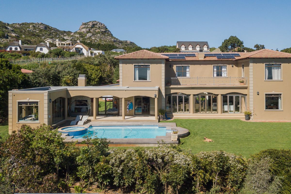 Aerial view of the rear elevation featuring a swimming pool, built-in jacuzzi, covered patio, balcony, and solar panels set within a landscaped garden.