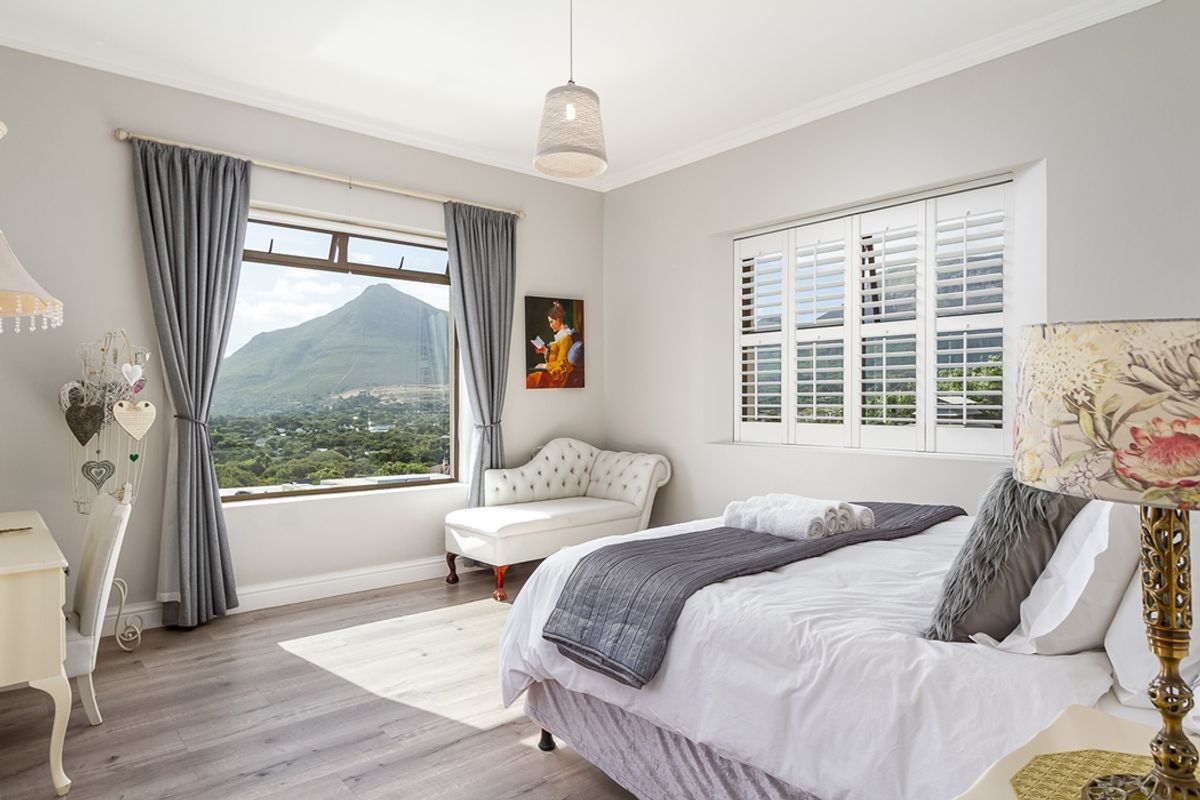 A bright and well-maintained bedroom featuring laminate flooring, plantation shutters, and a large window offering scenic mountain views.