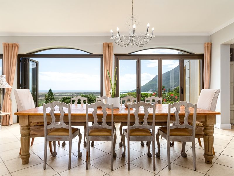 Spacious dining room featuring large arched folding doors that open to scenic mountain and coastal views, complemented by elegant tiled flooring and a classic chandelier.