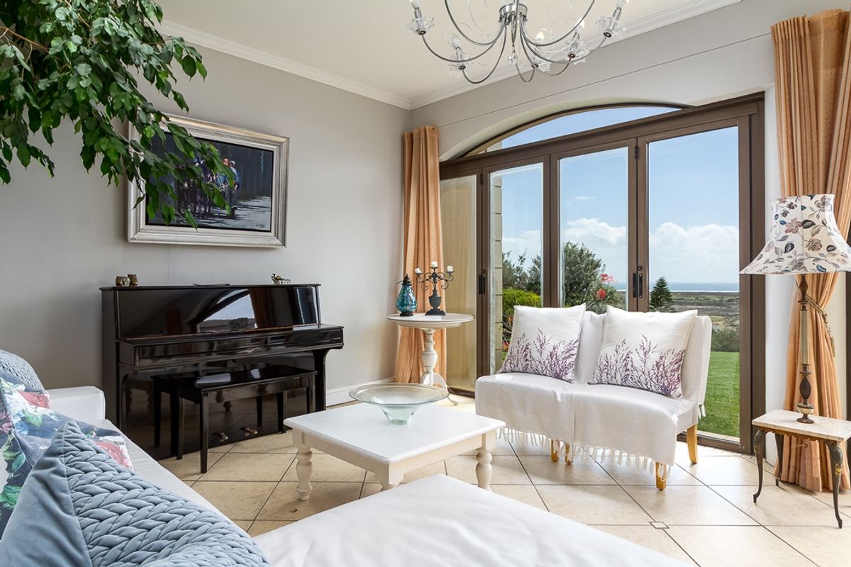 A bright living room featuring tiled flooring, elegant cove cornicing, and large arched glass doors that provide access to the garden and scenic views.