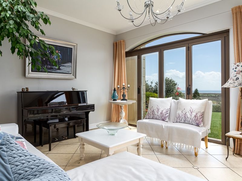 A bright living room featuring tiled flooring, elegant cove cornicing, and large arched glass doors that provide access to the garden and scenic views.