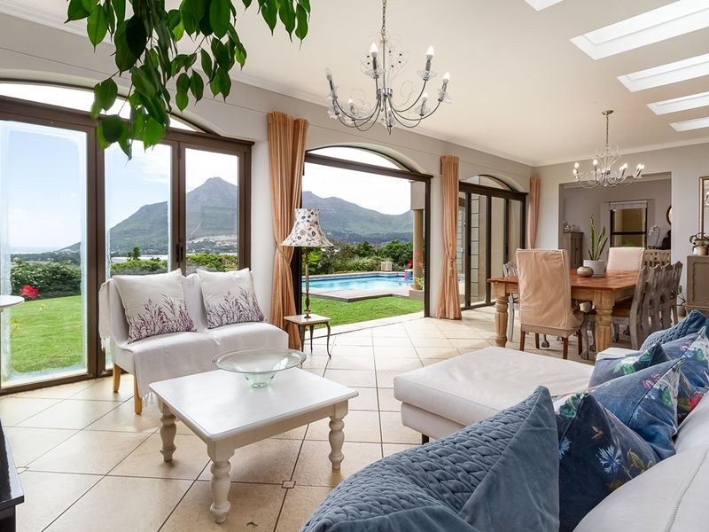 Spacious open-plan living and dining area featuring tiled floors, skylights, and large arch-top sliding doors opening to a garden and pool view.