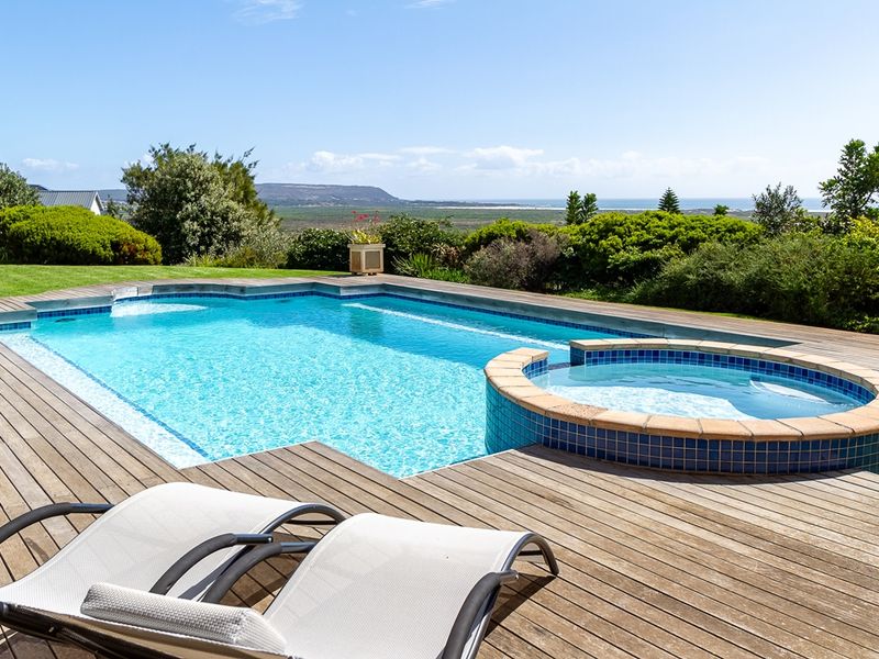 A well-maintained swimming pool and raised spa set within a timber deck, featuring expansive coastal and landscape views.