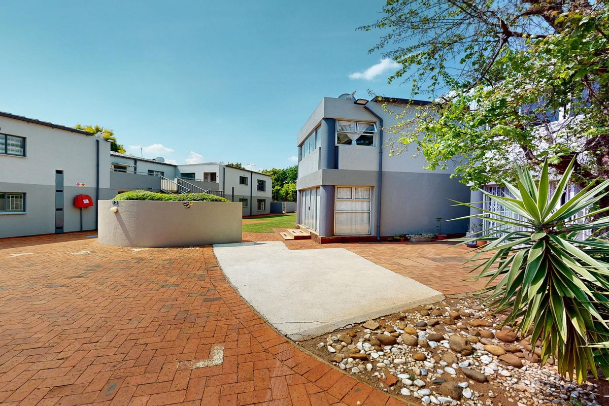 A view of the townhouse complex exterior featuring brick paved courtyard areas, concrete retaining walls, and multi-story residential units with security window bars.