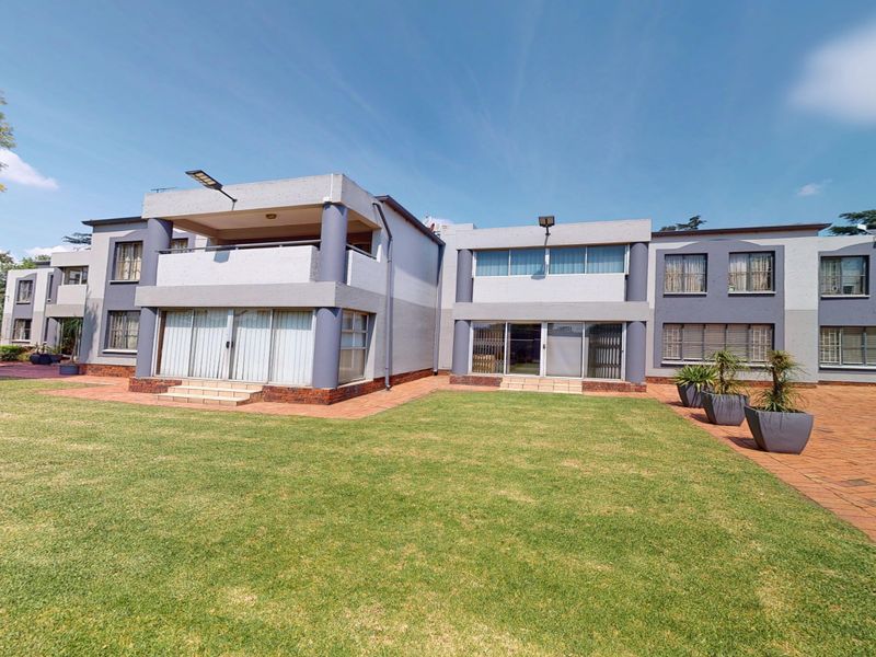 Rear view of the townhouse complex featuring a spacious lawn, brick paved patio areas, and upper-level balcony with sliding glass door access.