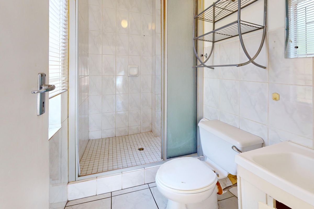 A compact bathroom featuring a shower enclosure, toilet, and vanity basin with tiled finishes, requiring some maintenance and cosmetic updates.