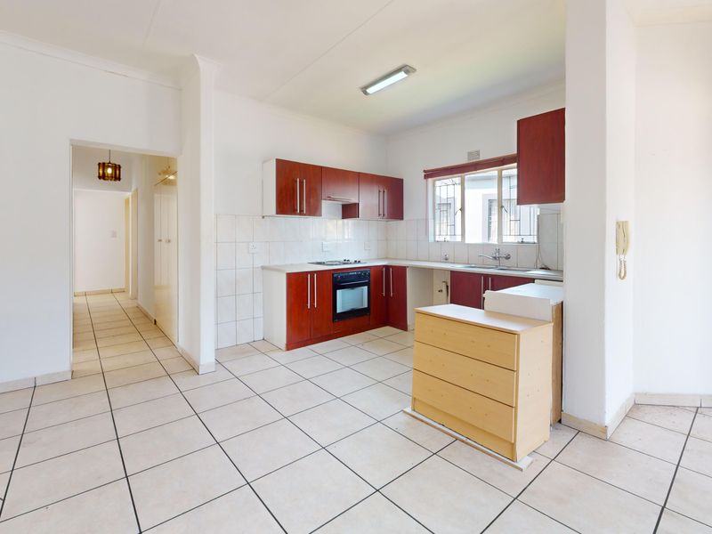 A functional kitchen featuring built-in cabinetry, a tiled backsplash, and integrated oven and hob, set within an open-plan layout with tiled flooring.