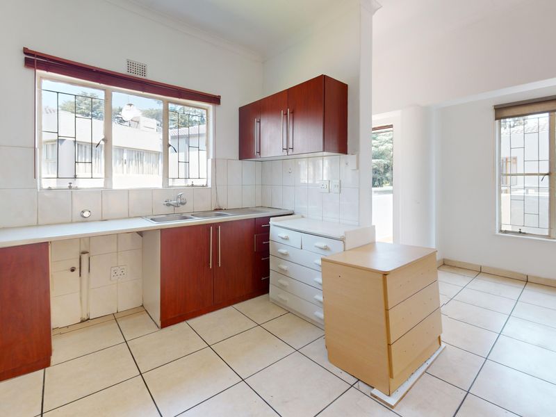 An open-plan kitchen area featuring built-in wooden cabinetry, tiled flooring, and a double sink, offering a functional space ready for modernization.