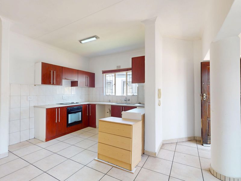 A functional kitchen featuring built-in wooden cabinetry, an integrated oven and hob, tiled flooring, and a double sink with a tiled backsplash.