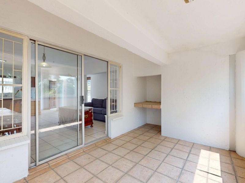 A covered patio area featuring tiled flooring, security bars on windows, and a built-in alcove shelf, providing a functional outdoor space.