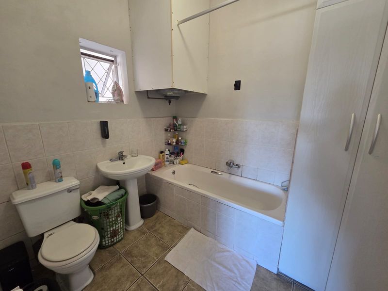 A functional bathroom featuring a pedestal basin, built-in bathtub, tiled finishes, and built-in storage cabinetry.