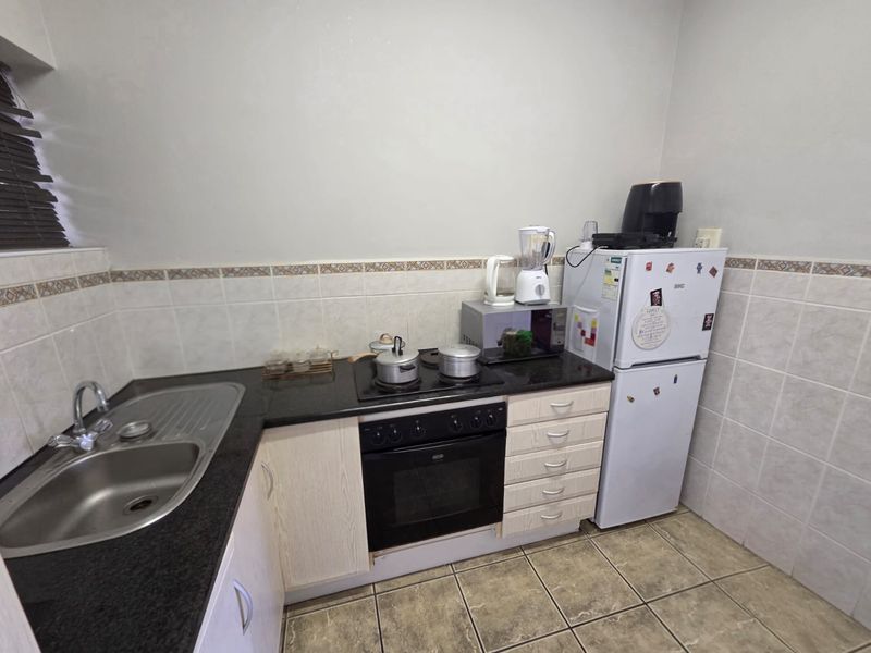 Compact kitchen featuring granite countertops, built-in oven with hob, stainless steel sink, and tiled finishes throughout.