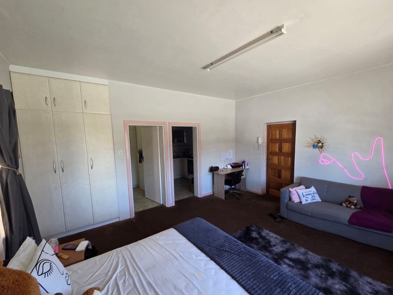 Spacious bedroom featuring built-in wardrobes, dark carpeting, and direct access to adjacent rooms through timber doors.