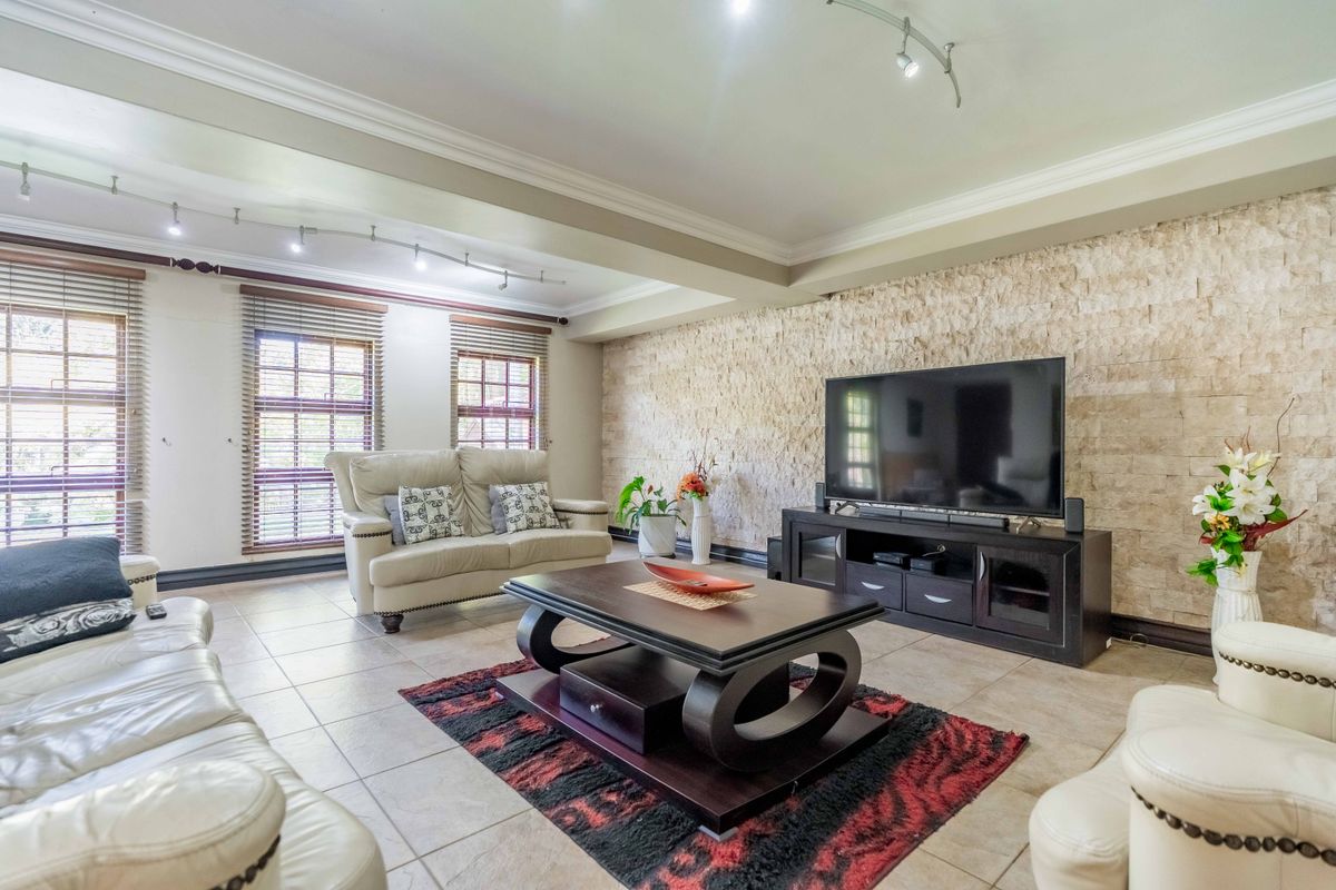 Spacious living room featuring a textured stone accent wall, neutral tiled flooring, and modern track lighting, creating a comfortable and inviting atmosphere.
