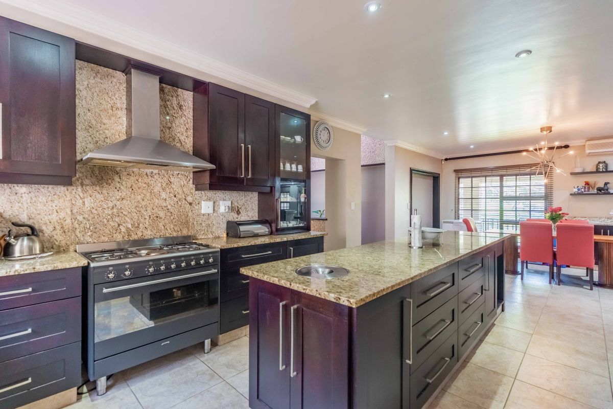Spacious kitchen featuring dark wood cabinetry, granite countertops, a central island with a prep sink, and a professional-style gas stove with an extractor fan.