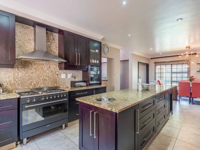 Spacious kitchen featuring dark wood cabinetry, granite countertops, a central island with a prep sink, and a professional-style gas stove with an extractor fan.
