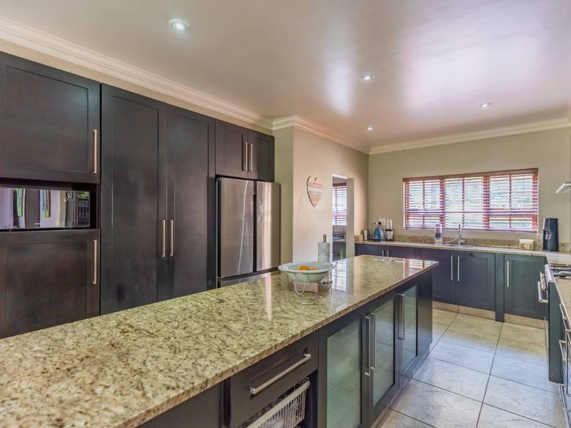 Modern kitchen featuring dark cabinetry, granite countertops, a central island, and high-quality built-in appliances with recessed lighting.