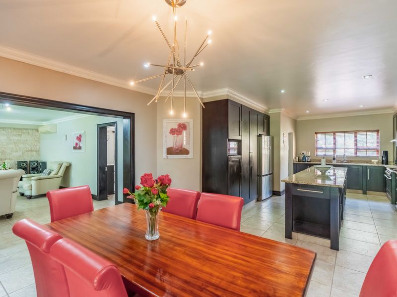 Spacious open-plan dining and kitchen area featuring dark cabinetry, granite countertops, a central island, and modern lighting fixtures with neutral tiled flooring throughout.